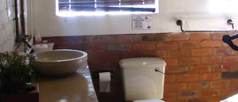 A bathroom with a large bowl sink, toilet, and a window with blinds.