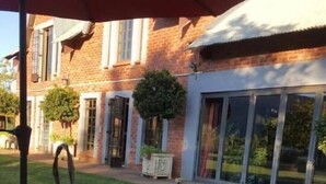 An outdoor dining area with a table set for a meal, surrounded by a brick building and a glass door. - Millstream Inn Guesthouse (Hartbeespoort)