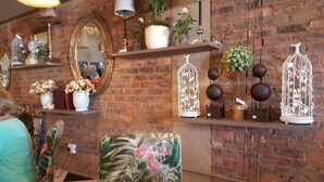 A room with brick walls, a mirror, and shelves with decorative items including vases, plants, and birdcages. - Millstream Inn Guesthouse (Hartbeespoort)