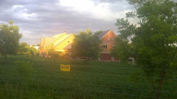 A rural property with a large field, a building with a yellow roof, and a sign in the foreground. - Millstream Inn Guesthouse (Hartbeespoort)