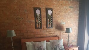 A hotel room with a brick wall, a wooden bed, two nightstands with lamps, and a chair. - Millstream Inn Guesthouse (Hartbeespoort)