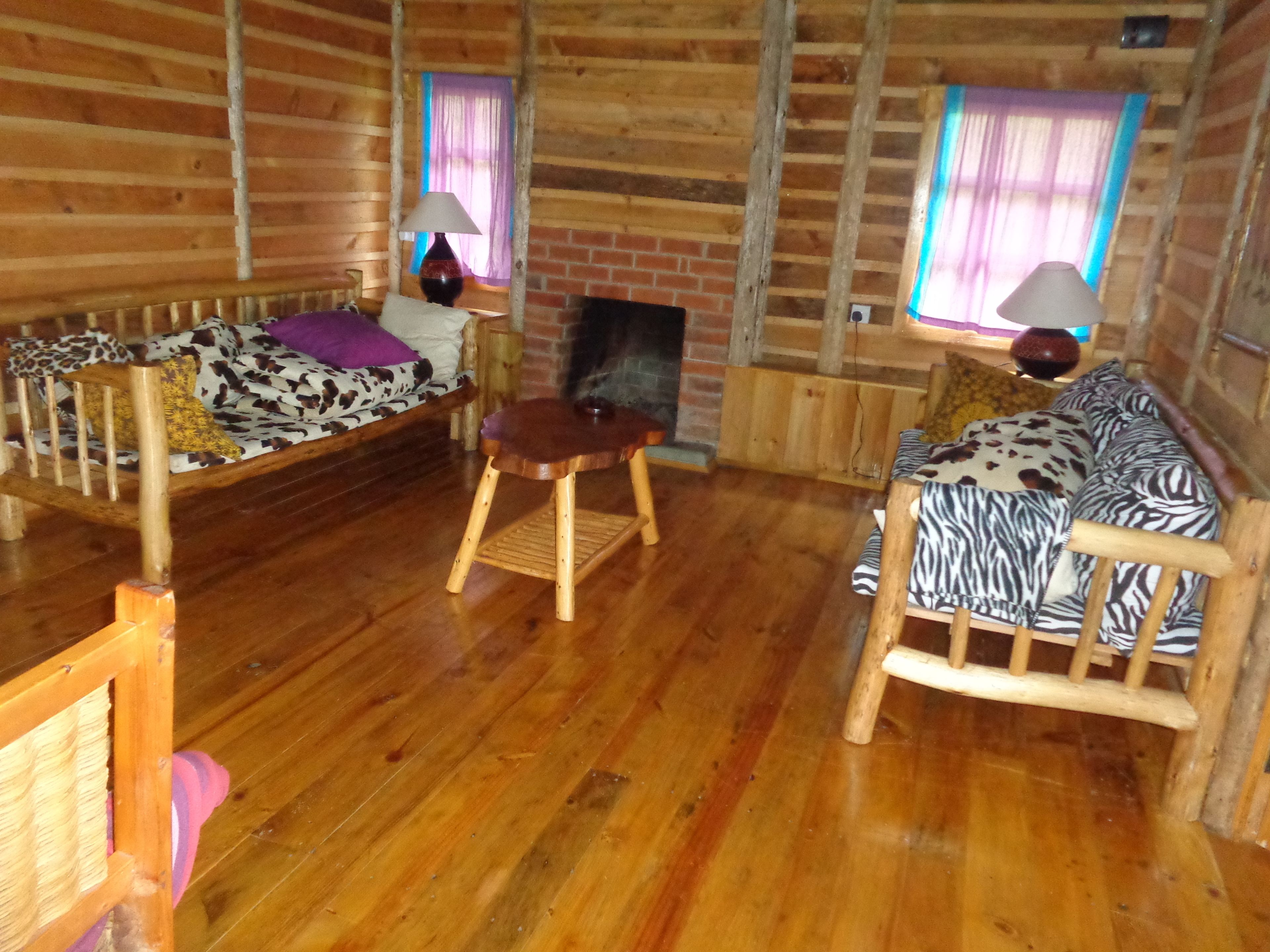 L’intérieur d’une cabane en rondins, avec un plancher en bois, un canapé à motifs zébrés, une chaise en bois et une petite table sur laquelle se trouve une lampe.