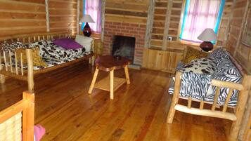 L’intérieur d’une cabane en rondins, avec un plancher en bois, un canapé à motifs zébrés, une chaise en bois et une petite table sur laquelle se trouve une lampe.