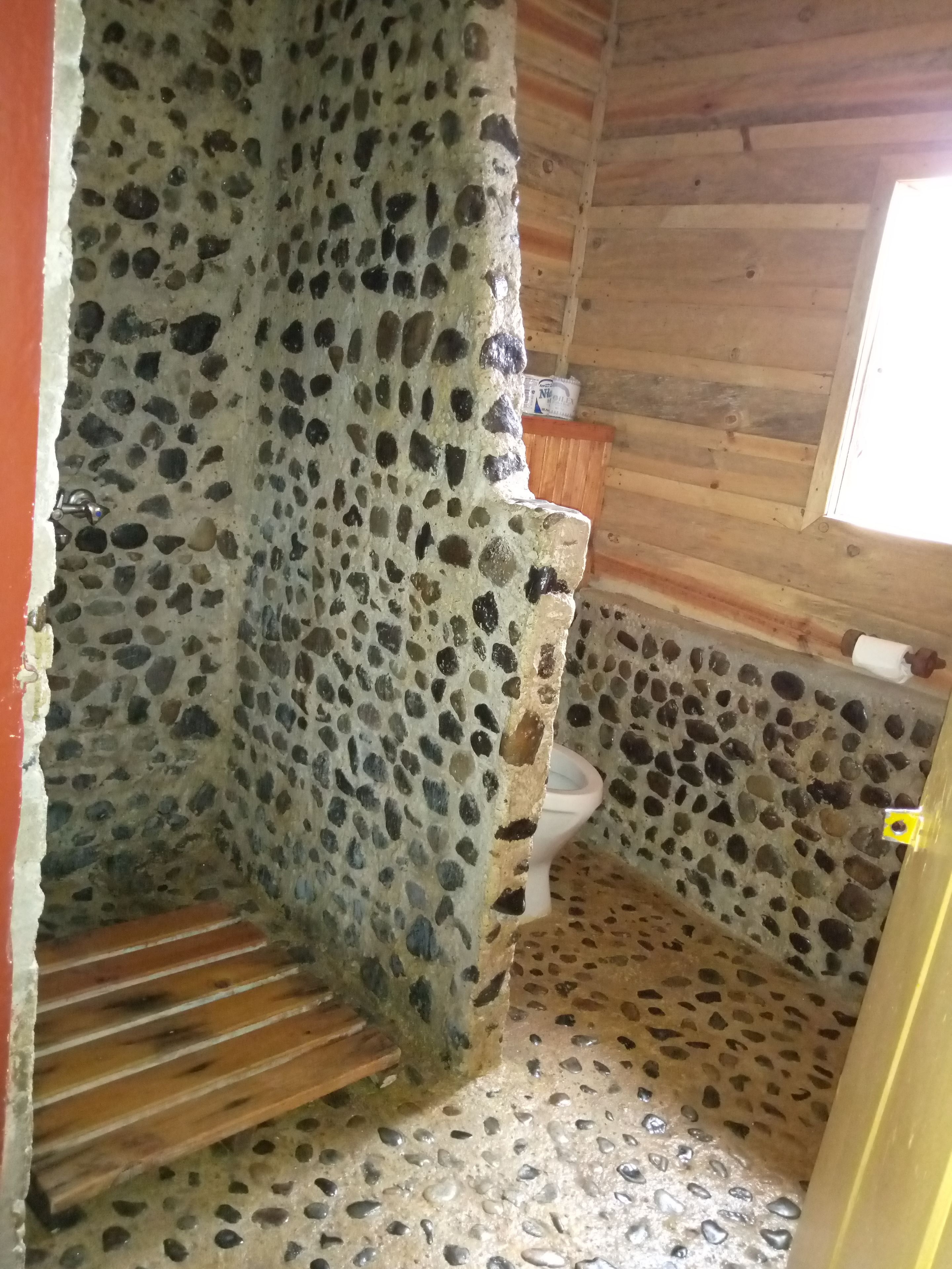 Ein Badezimmer mit Steinwand, Holzboden und Toilette.
