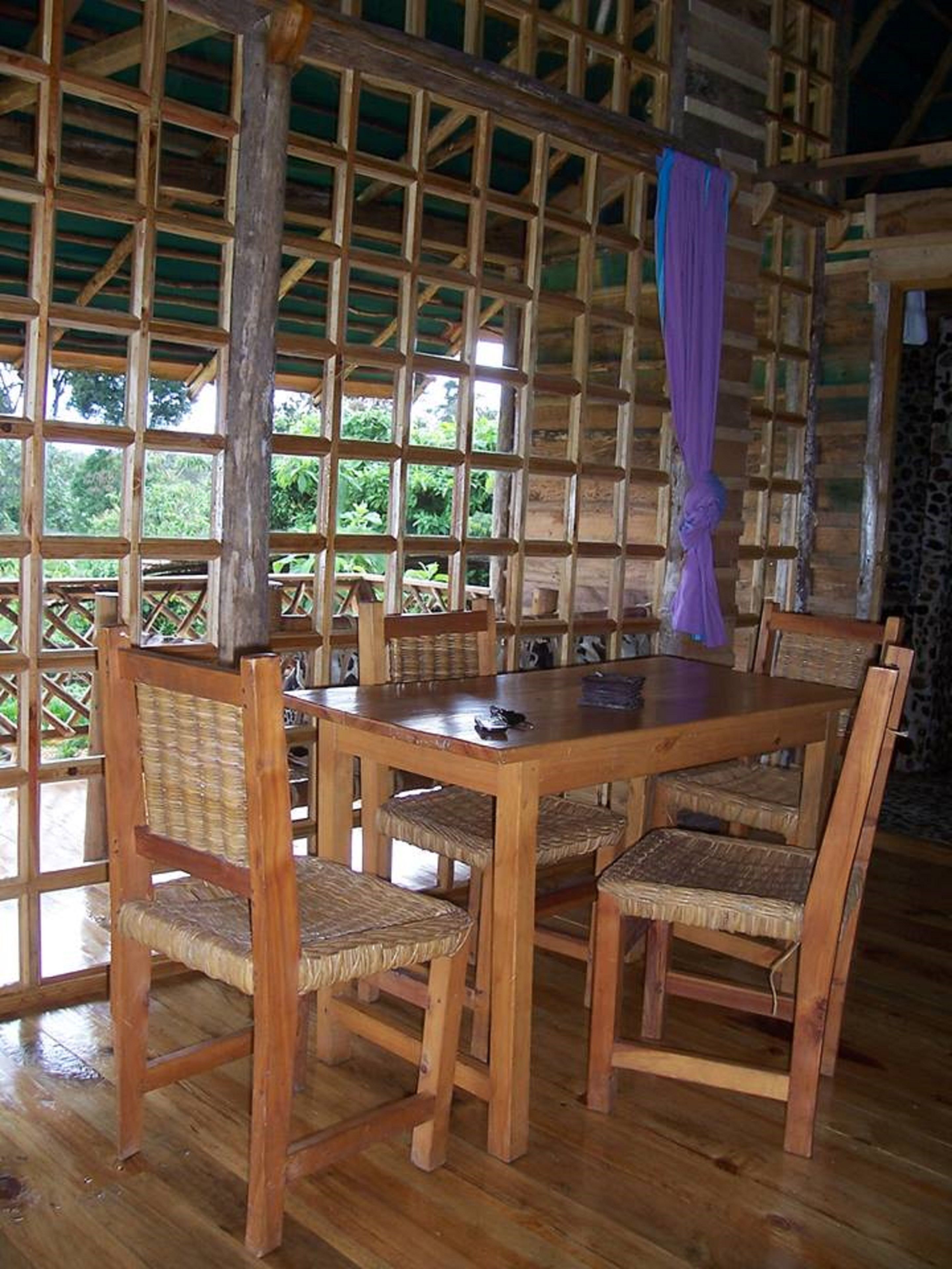 A wooden dining table with four chairs, surrounded by a wooden lattice wall with a view of greenery outside.