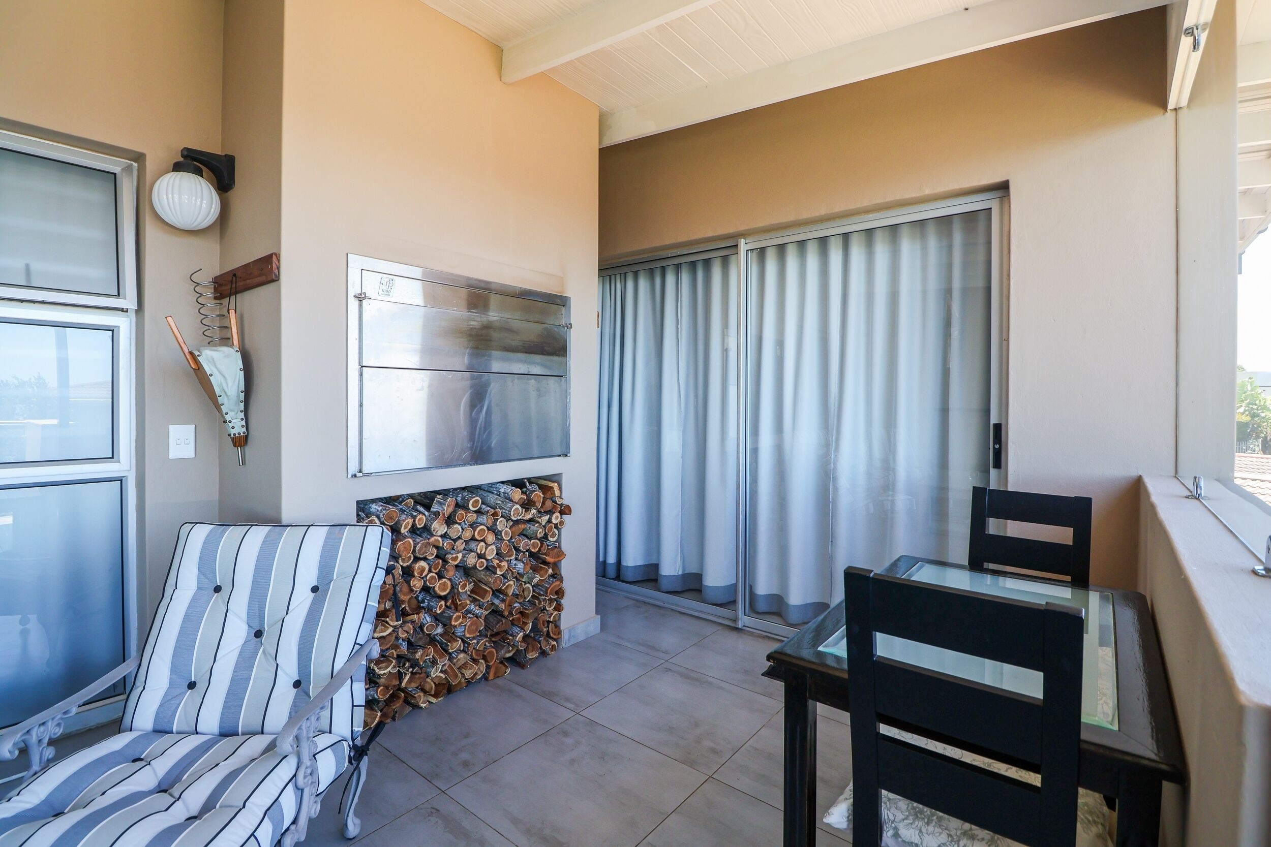 A balcony with a cushioned chair, a table, and a stack of firewood.
