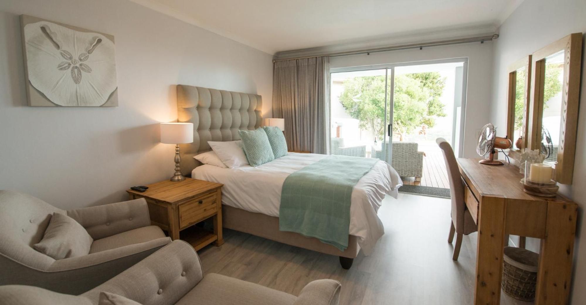 A bedroom with a bed, bedside table, lamp, chair, and a view of the outdoors.
