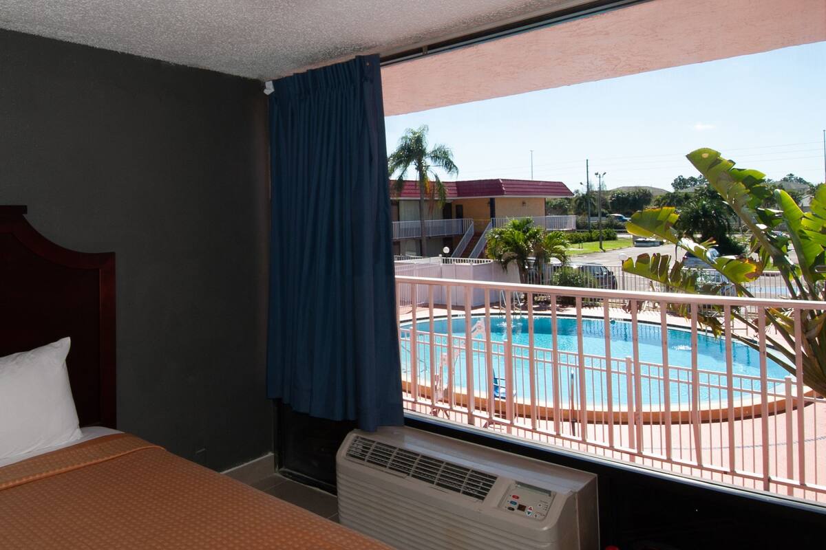 A hotel room with a bed, an air conditioner, and a view of a swimming pool.