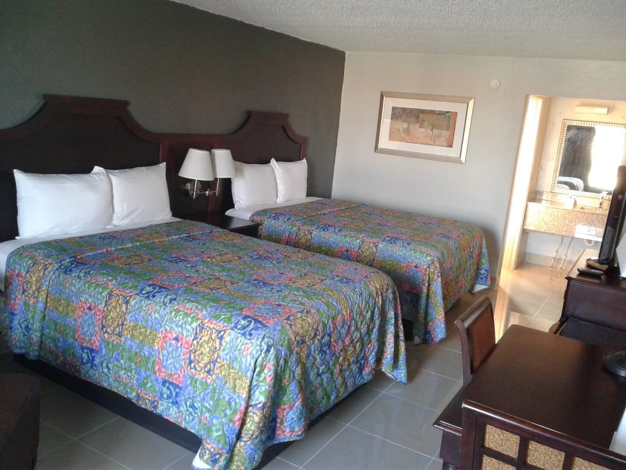 Habitación de hotel con dos camas, un escritorio, una silla y un televisor.