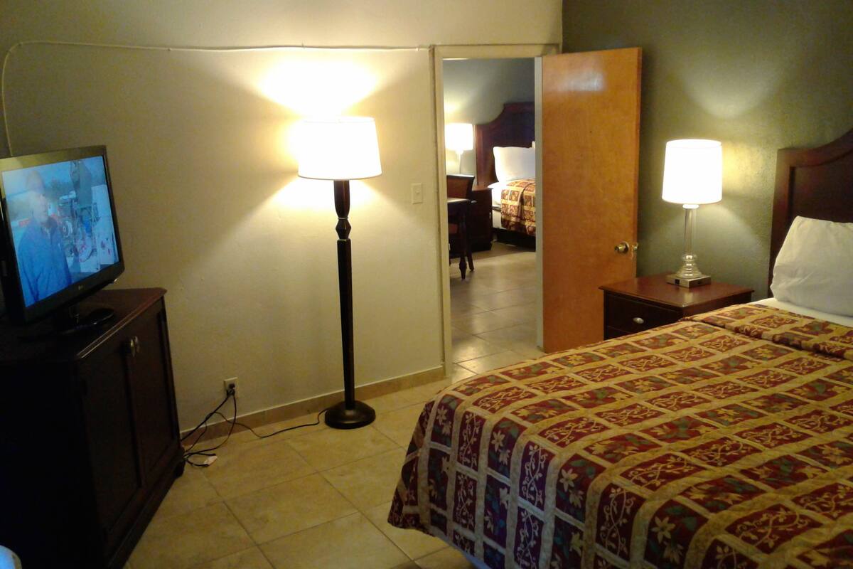 A hotel room with a bed, a television, two bedside lamps, and a door leading to another room.