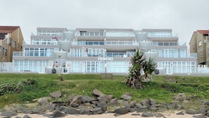 Un hôtel moderne à plusieurs étages, avec une enseigne bien visible portant le nom « TONTIKI », et une plage de sable avec des rochers au premier plan.