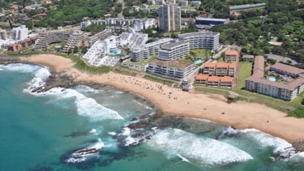 Vue aérienne d’une zone côtière comprenant une plage, plusieurs immeubles de grande hauteur et un mélange de bâtiments résidentiels et commerciaux.