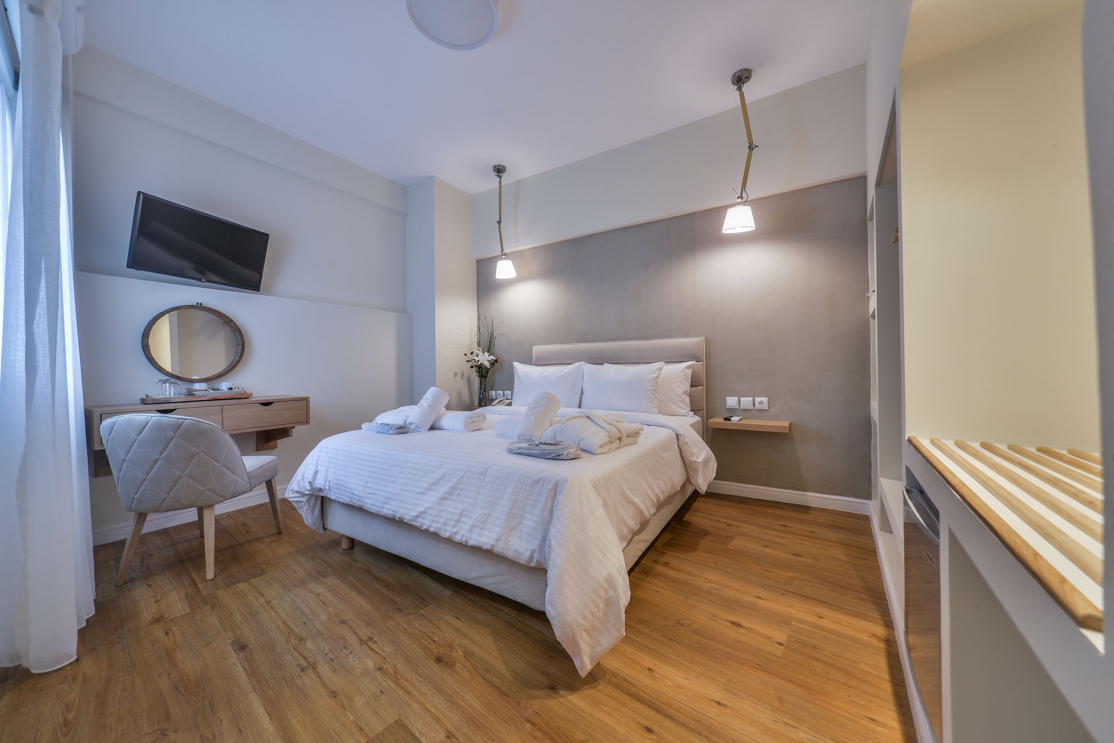 A modern bedroom with a bed, bedside table, chair, TV, and wooden flooring.