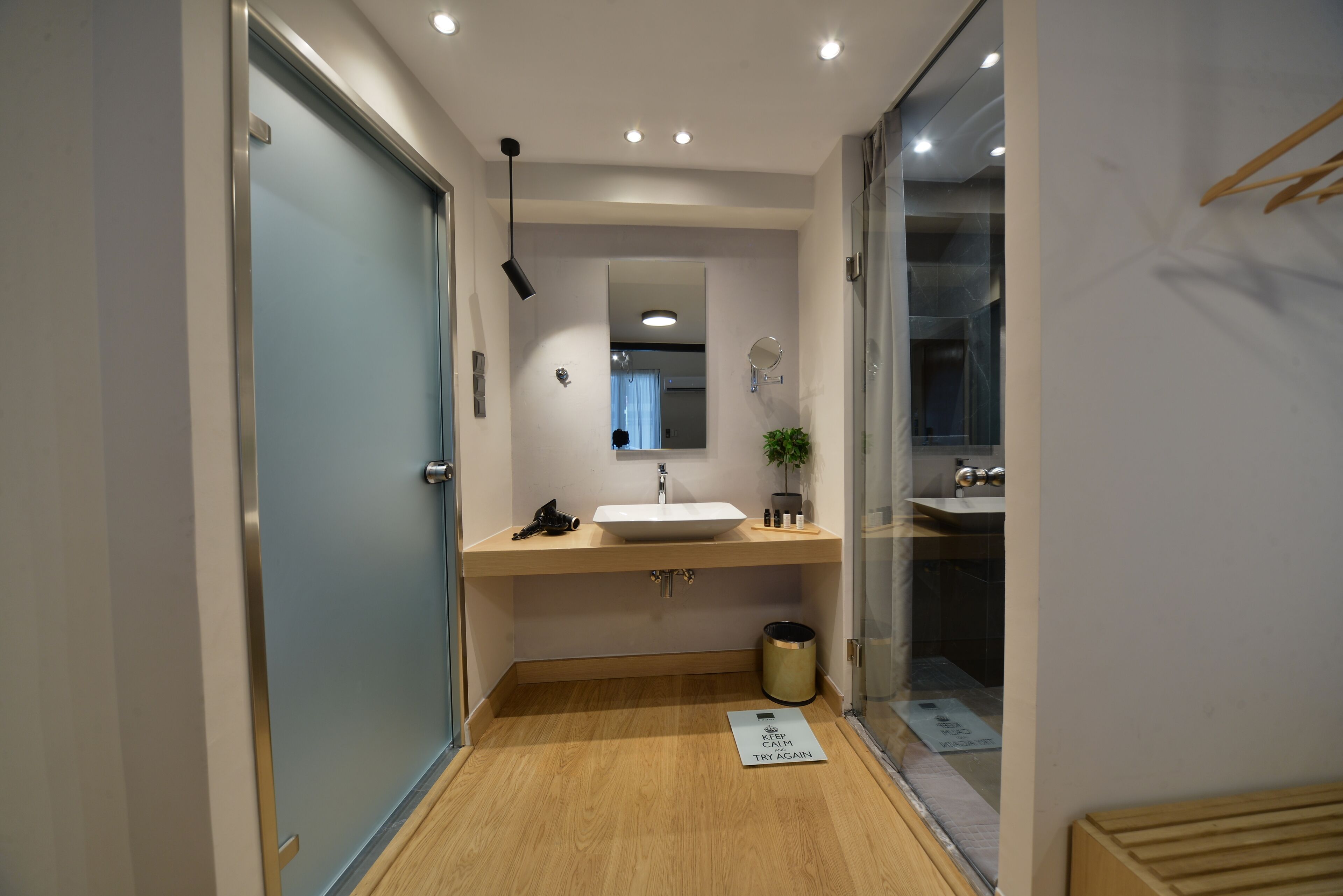 Un baño moderno con suelo de madera, un lavabo blanco, un espejo y un pequeño cubo de basura.