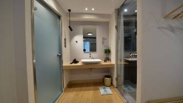 Un baño moderno con suelo de madera, un lavabo blanco, un espejo y un pequeño cubo de basura.