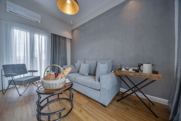 A modern living room with a grey sofa, a wooden coffee table, a wicker basket, and a grey armchair. - A.P. Acropolis View Apartments (Athens)