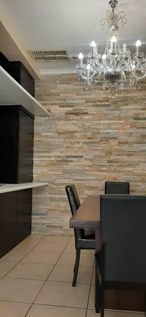 A dining area with a stone wall, a chandelier, and a TV mounted on the wall. - Two Normal Bedrooms Inside Maerua Mall (Windhoek)