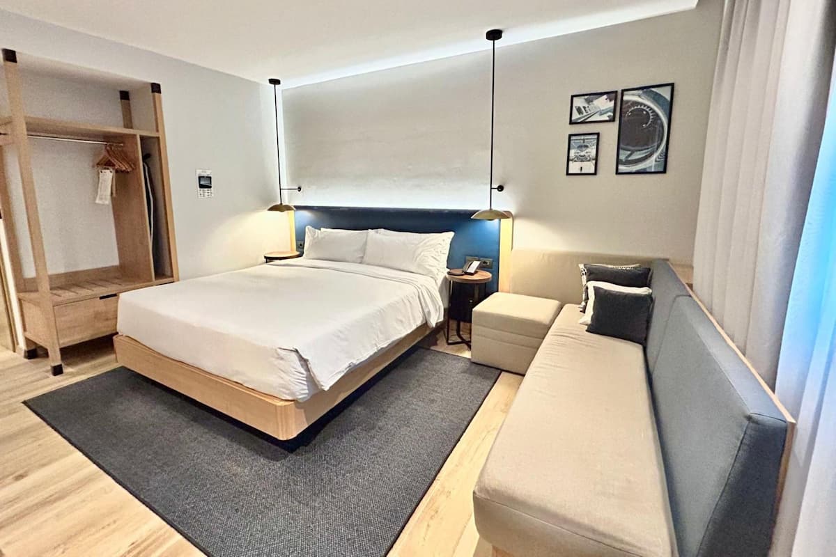 Una habitación de hotel moderna con una cama grande, mesitas de noche, un sofá, un armario de madera y un escritorio pequeño.