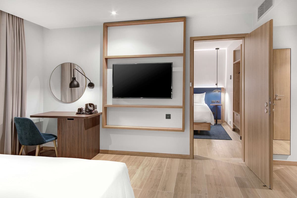 Una habitación de hotel con cama, escritorio con silla, televisor montado en la pared y armario.