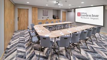 A conference room with a long table, grey chairs, a projector screen, and a carpeted floor.