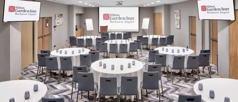 Un salón de conferencias con múltiples mesas redondas, cada una con sillas, en Hilton Garden Inn Bucharest Airport.