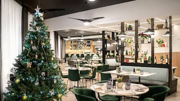 A modern dining area with green upholstered chairs, a Christmas tree, and a bar area in the background.