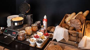 Un buffet de petit-déjeuner proposant une variété d’aliments, une machine à gaufres et des condiments.
