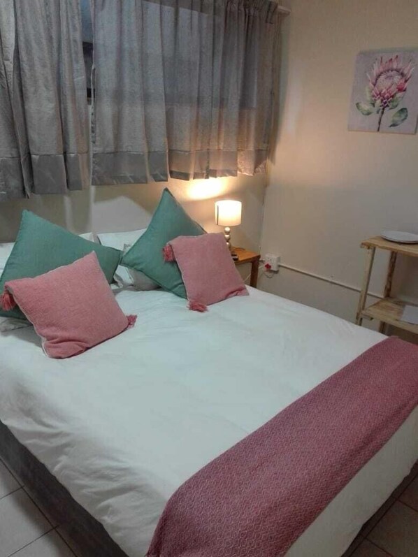 A bed with white bedding, green and pink pillows, and a pink throw.