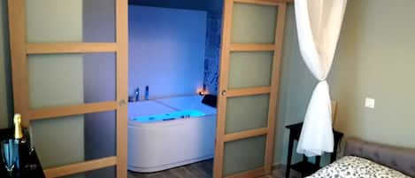 Quarto com uma cama grande, mesa de cabeceira, banheira com iluminação azul e estrutura de dossel sobre a cama.