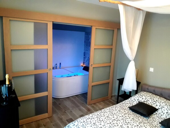 Un dormitorio con una cama grande, una mesita de noche, una bañera y un dosel sobre la cama, con iluminación azul.