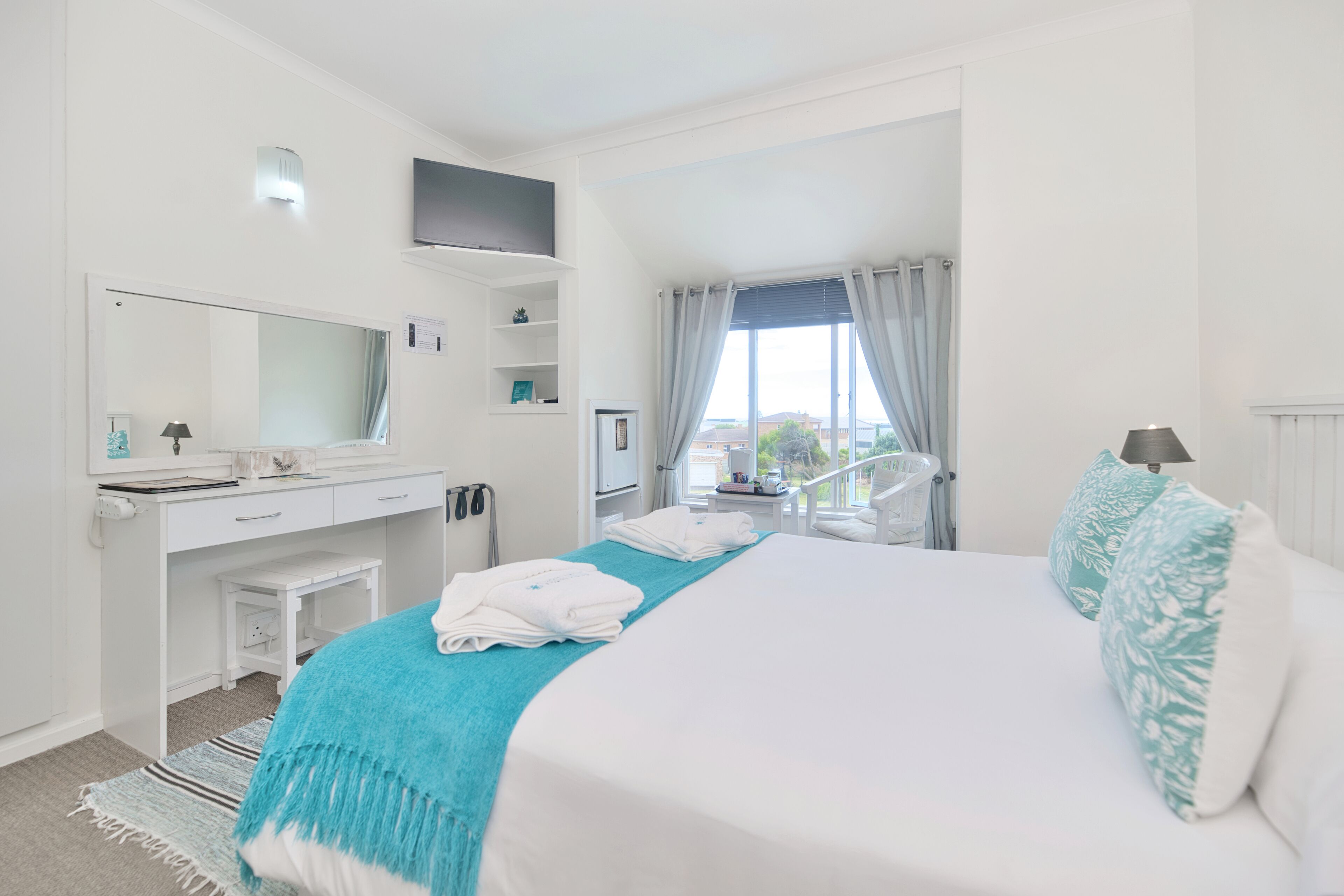 A hotel room with a bed, a desk, a chair, a TV, and a window with curtains.