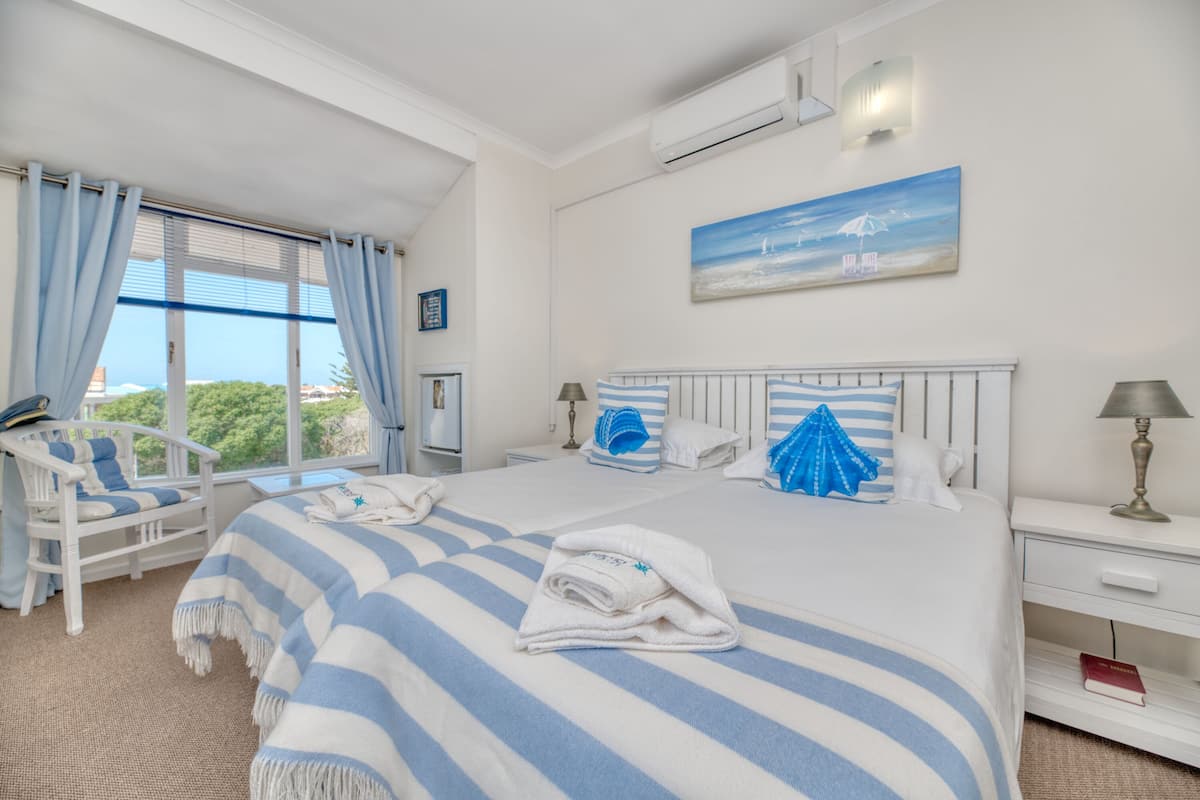 A hotel room with a large bed, a chair, a bedside table, and a window with curtains.