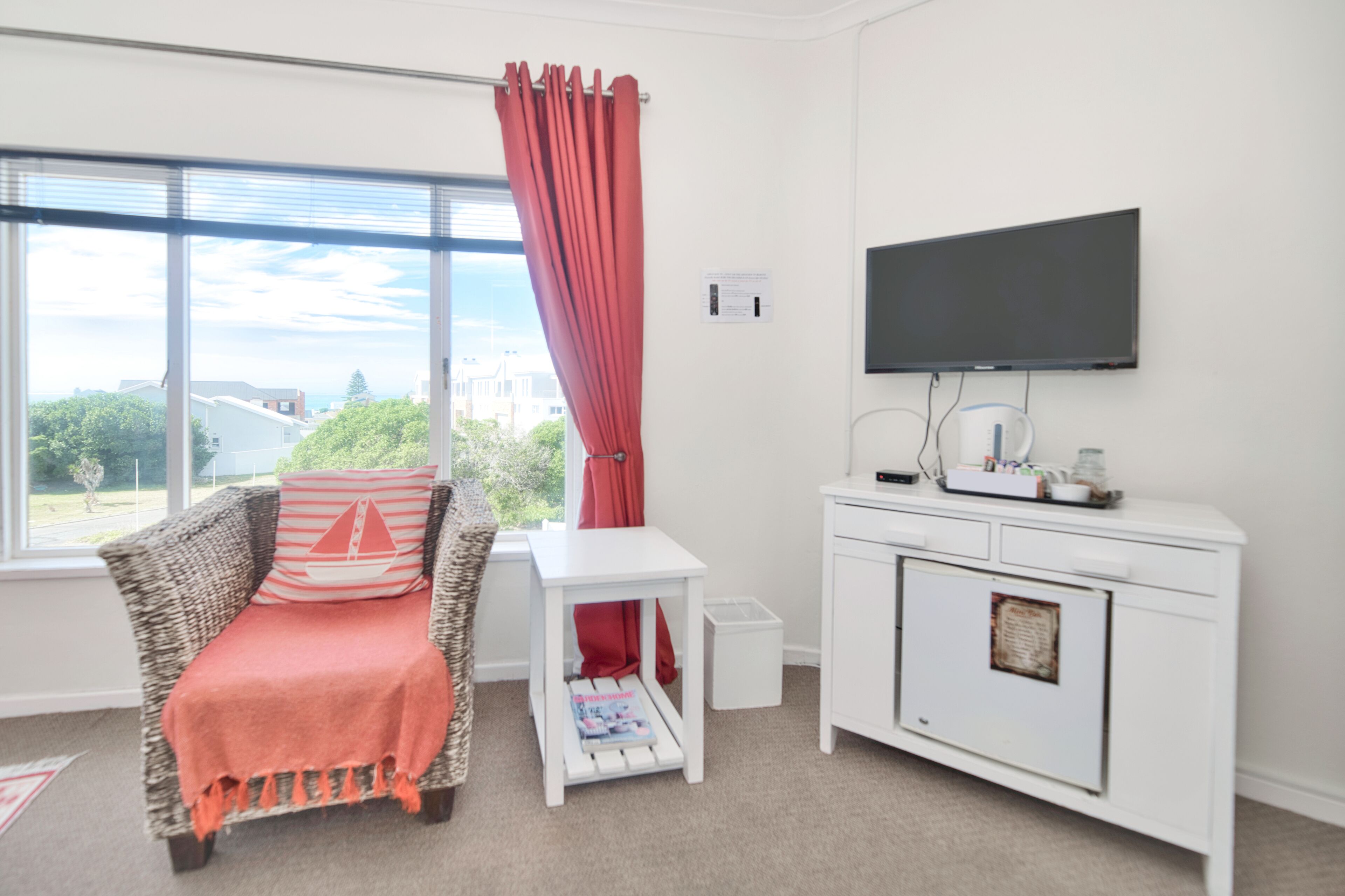 A room with a wicker sofa, a white cabinet, a television, and a window with a view of buildings and trees.