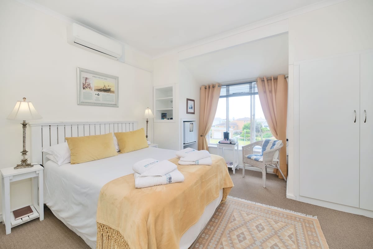 A hotel room with a bed, bedside table, lamp, and a view of the outside.