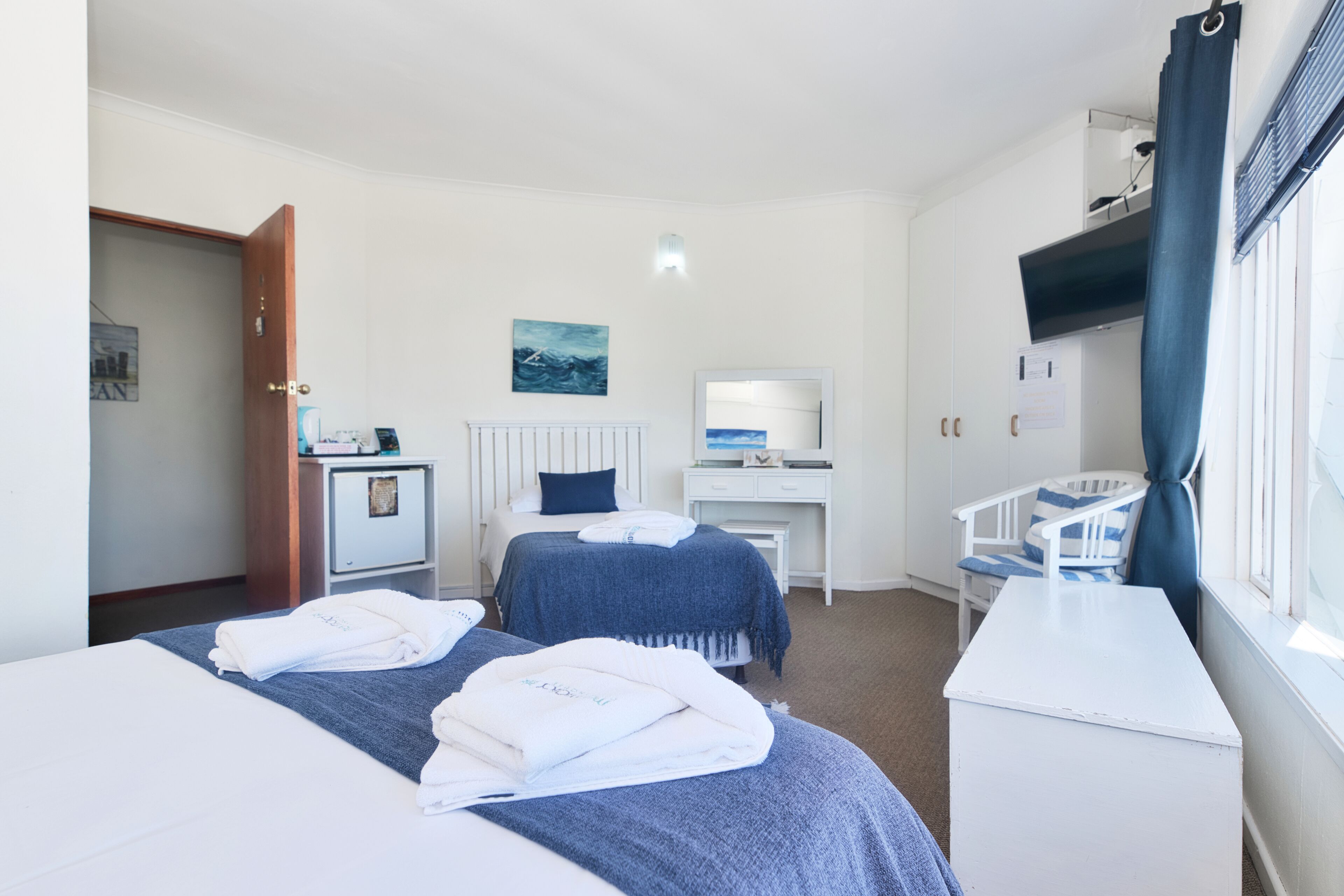 A hotel room with two beds, a desk, a chair, and a window with curtains.