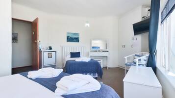 A hotel room with two beds, a desk, a chair, and a window with curtains.