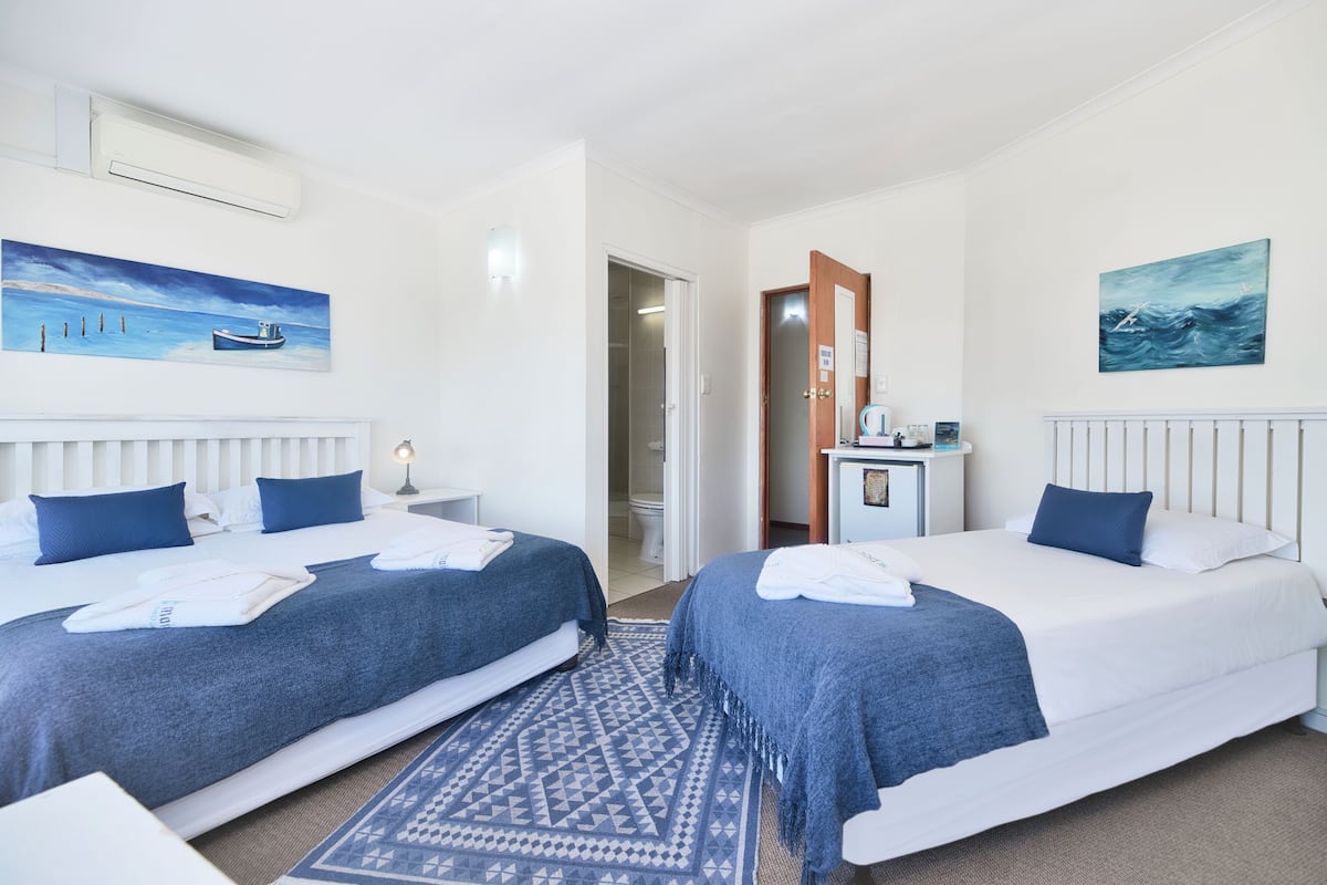 A hotel room with two beds, a desk, and a bathroom visible through an open door.
