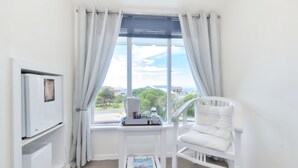 Ein Zimmer mit einem weißen Stuhl, einem kleinen Tisch mit einer Zeitschrift und einem Fenster mit Vorhängen.