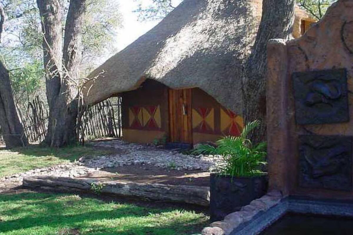 A thatched-roof structure with a patterned door, surrounded by trees and a stone pathway.