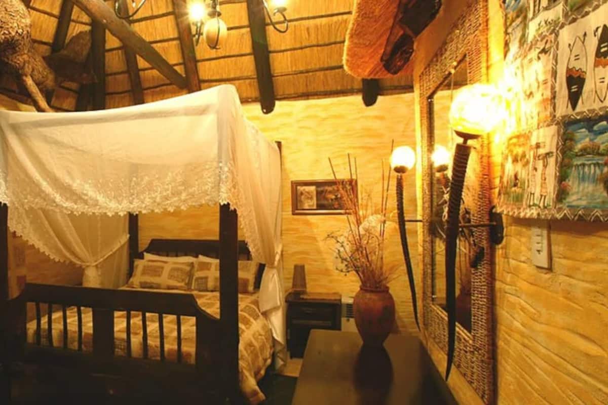 A rustic room with a wooden bed, a chair, a table, and a wall with artwork.