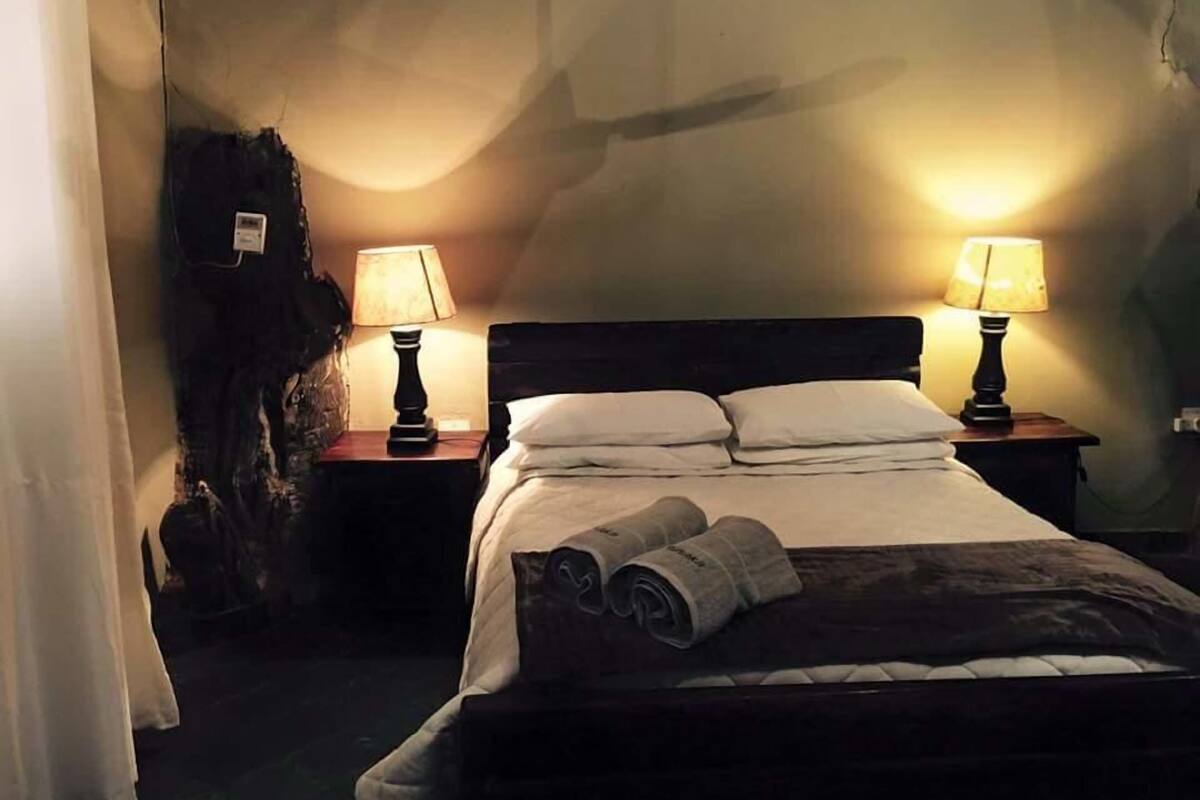 A hotel room with a bed, two bedside lamps, a nightstand, and a curtain.