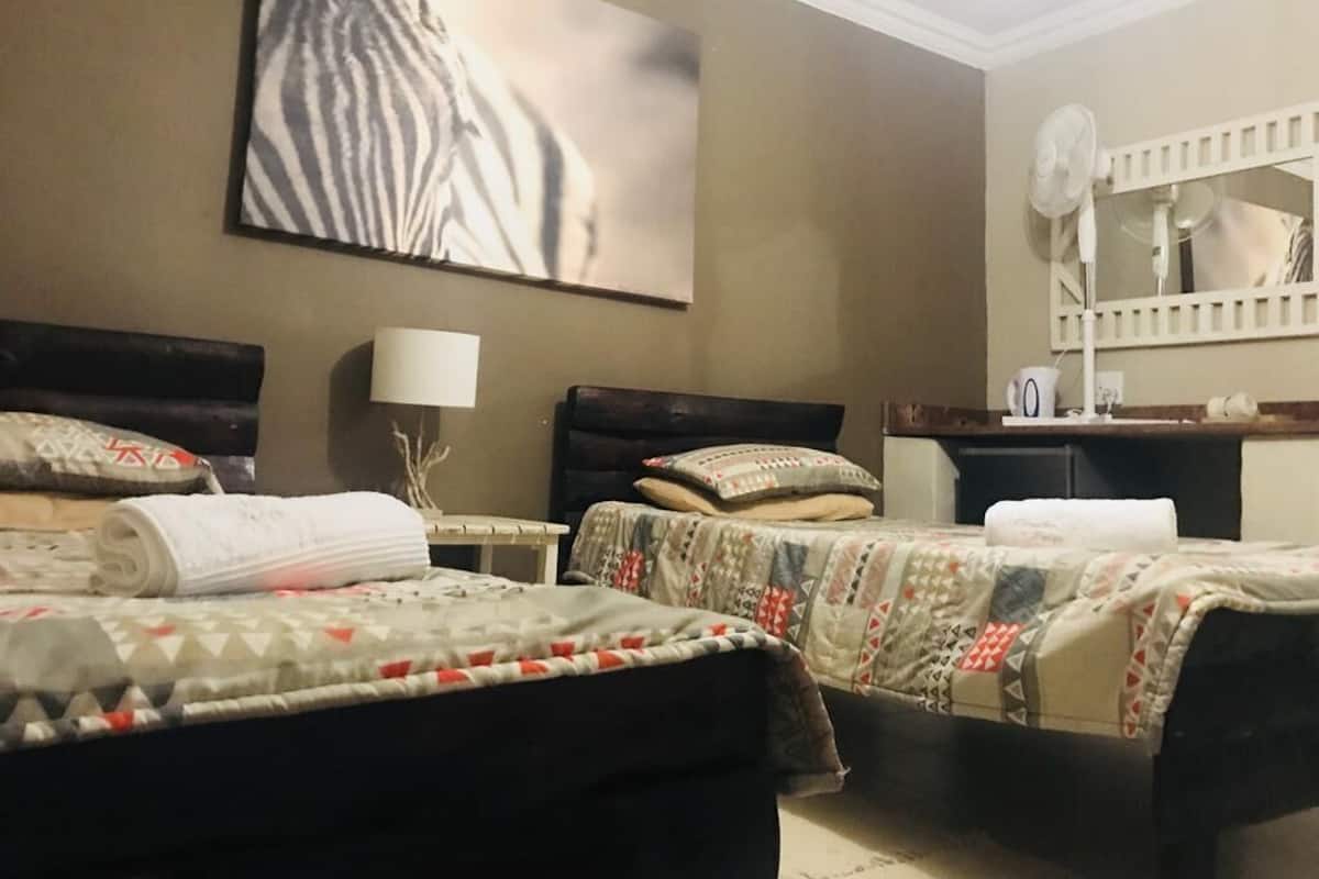 A hotel room with two beds, a large abstract painting, a mirror, and a bedside table with a lamp.