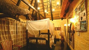 A rustic room with a wooden bed, a chair, a table, and a wall with artwork. - Chinaka Game Lodge (Vivo)