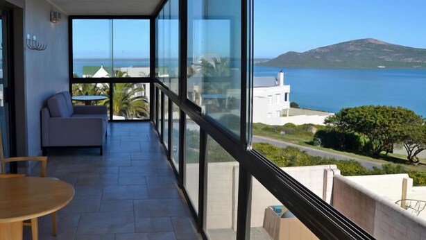 A balcony with a view of the sea and a mountain, a sofa, and a table. - Kite Mansion Penthouse (Langebaan)