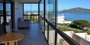 A balcony with a view of the sea and a mountain, a sofa, and a table.