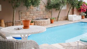 A pool area with a stone wall, potted plants, and white lounge chairs. - Kite Mansion Penthouse (Langebaan)