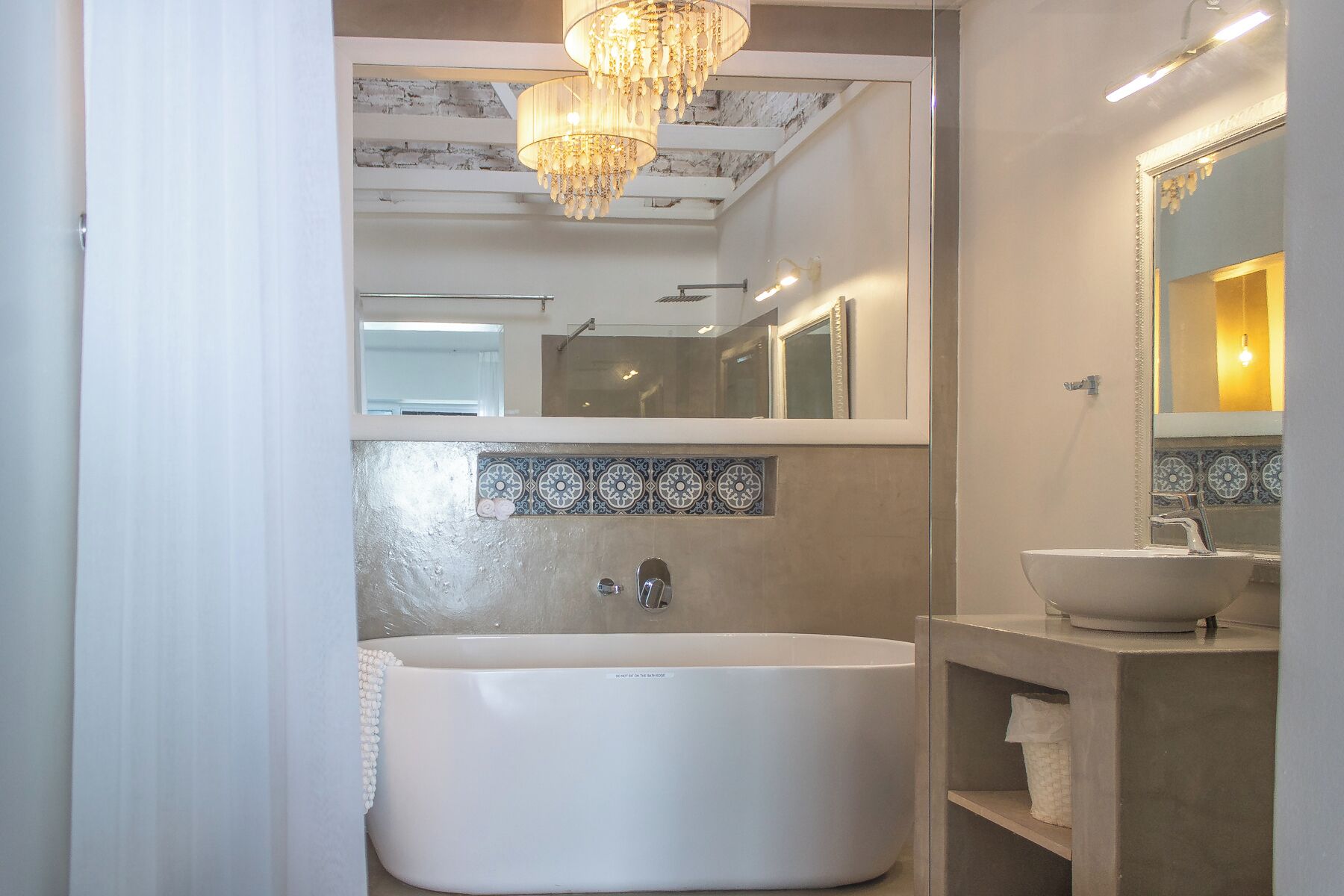 A modern bathroom with a freestanding bathtub, a large mirror, and a chandelier.