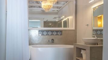 A modern bathroom with a freestanding bathtub, a large mirror, and a chandelier.