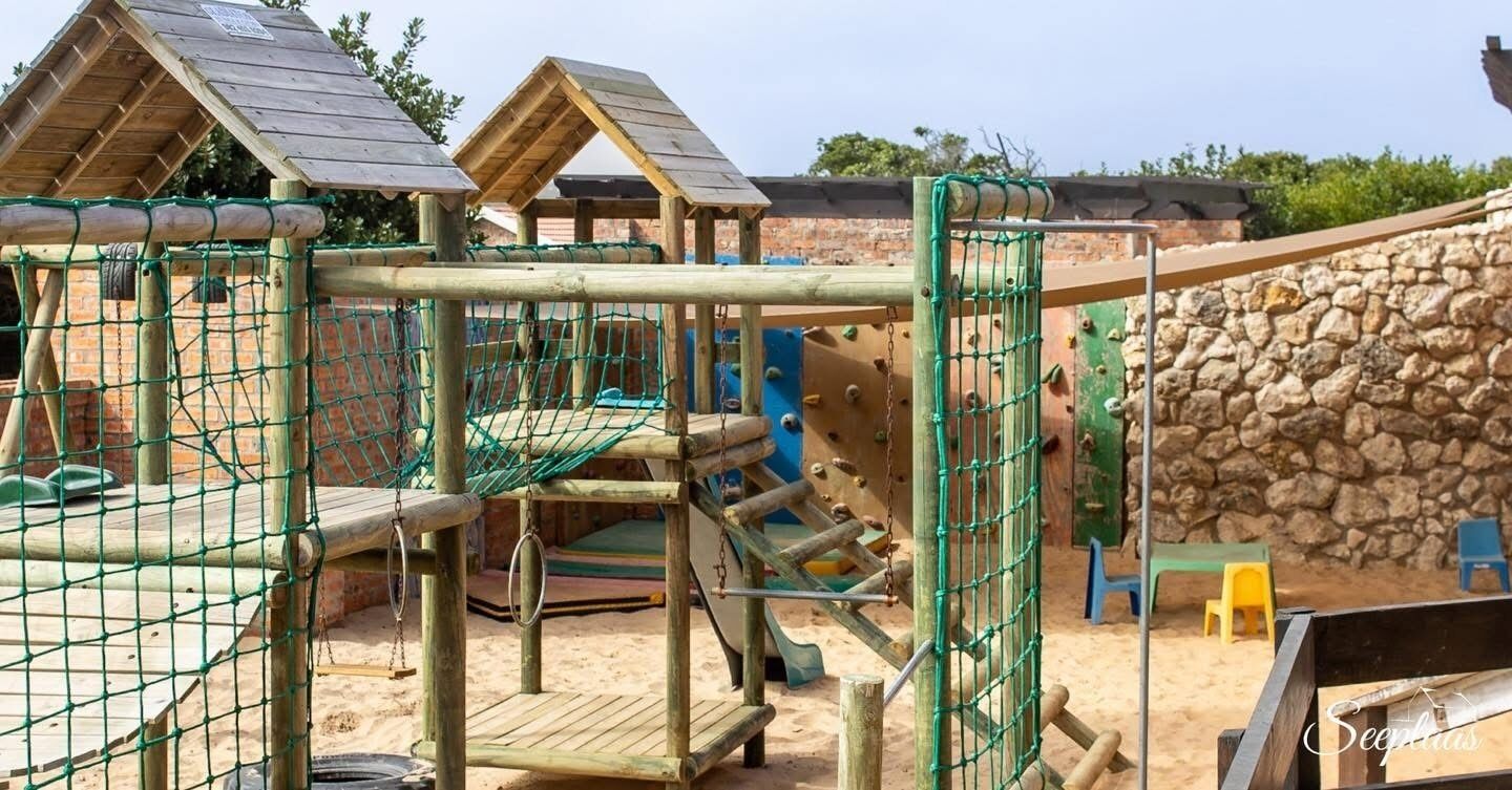 Un parque infantil con estructuras para escalar, una zona con red y un muro de piedra.