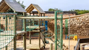 Un parque infantil con estructuras para escalar, una zona con red y un muro de piedra.